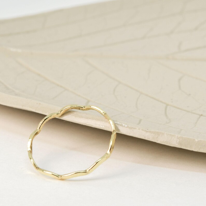May include: A delicate gold ring with a wavy, organic design. The ring is made of a thin band of metal and has a simple, elegant look.