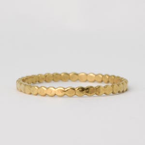 May include: A thin gold band ring with a textured, beaded design.