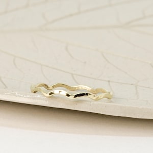May include: A thin gold ring with a wavy design. The ring is simple and delicate.