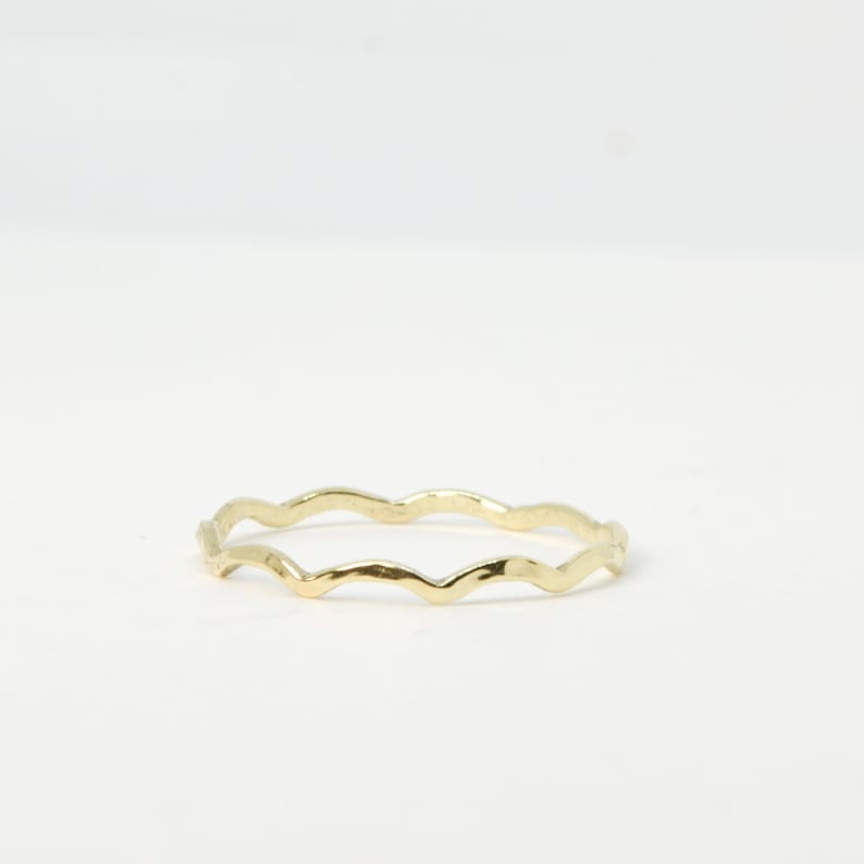 May include: A thin gold ring with a wavy, textured band.