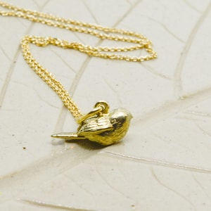 Op de afbeelding: Een gouden ketting met een klein, gedetailleerd gouden vogeltje als hanger.
