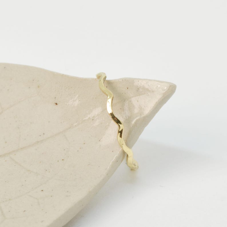 May include: A thin gold band ring with a wavy, textured design.