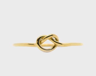 Puede incluir: Un anillo de nudo de oro con un diseño simple. El anillo está hecho de una banda delgada de metal y presenta un nudo en el centro.