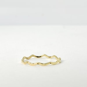 May include: A thin gold ring with a wavy, uneven edge.