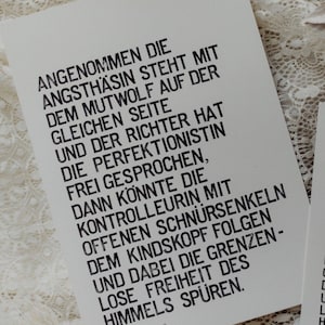 Könnte beinhalten: Zwei weiße Kunstdrucke mit schwarzem Text. Die Drucke zeigen ein Zitat auf Deutsch. Der größere Druck befindet sich links, ein kleinerer rechts. Der Hintergrund ist eine weiße, strukturierte Oberfläche.
