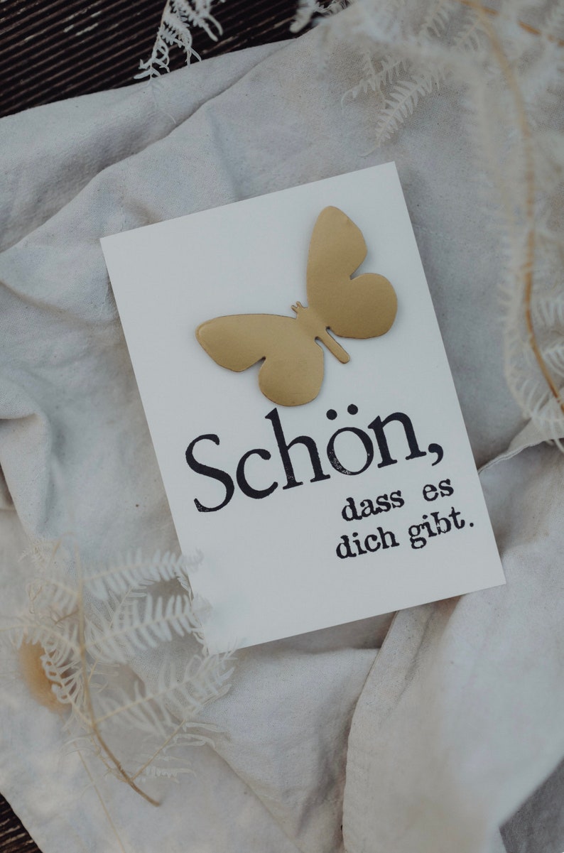 May include: A white card with a gold butterfly cutout and the text "Sch&ouml;n, dass es dich gibt."