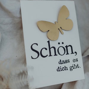 May include: A white card with a gold butterfly cutout and the text "Sch&ouml;n, dass es dich gibt." in black lettering.