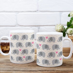May include: Two white ceramic mugs with a pattern of gray elephants and pink hearts. The mugs have a white background and a beige chevron pattern.