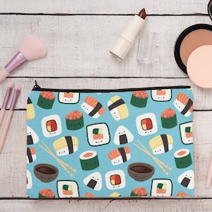 Puede incluir: Una bolsa de maquillaje azul con cremallera con un patrón de rollos de sushi y palillos. Los rollos de sushi tienen caras sonrientes y son de varios estilos, incluyendo nigiri, maki y sashimi.
