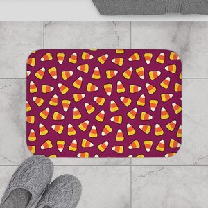 May include: A purple bath mat with a repeating pattern of yellow and orange candy corn.
