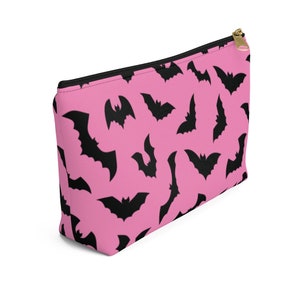 May include: A pink zippered pouch with a black bat pattern. The pouch is made of a soft, durable fabric and has a zipper closure.