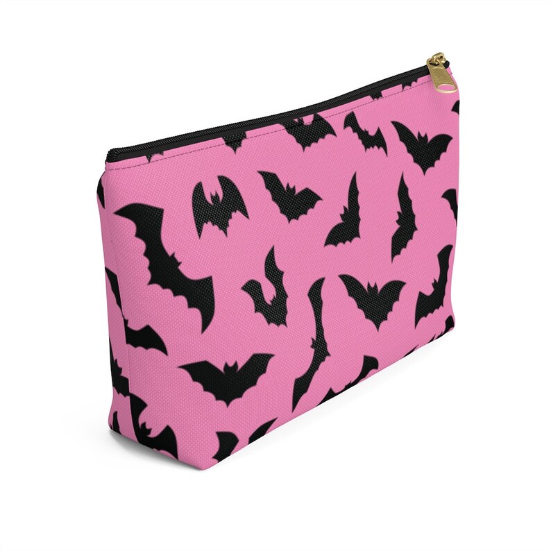 May include: A pink zippered pouch with a black bat pattern. The pouch is made of a soft, durable fabric and has a zipper closure.