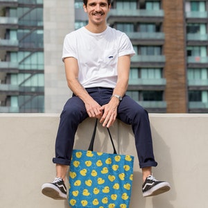 May include: A person sitting on a wall holding a blue tote bag with a yellow rubber ducky pattern.