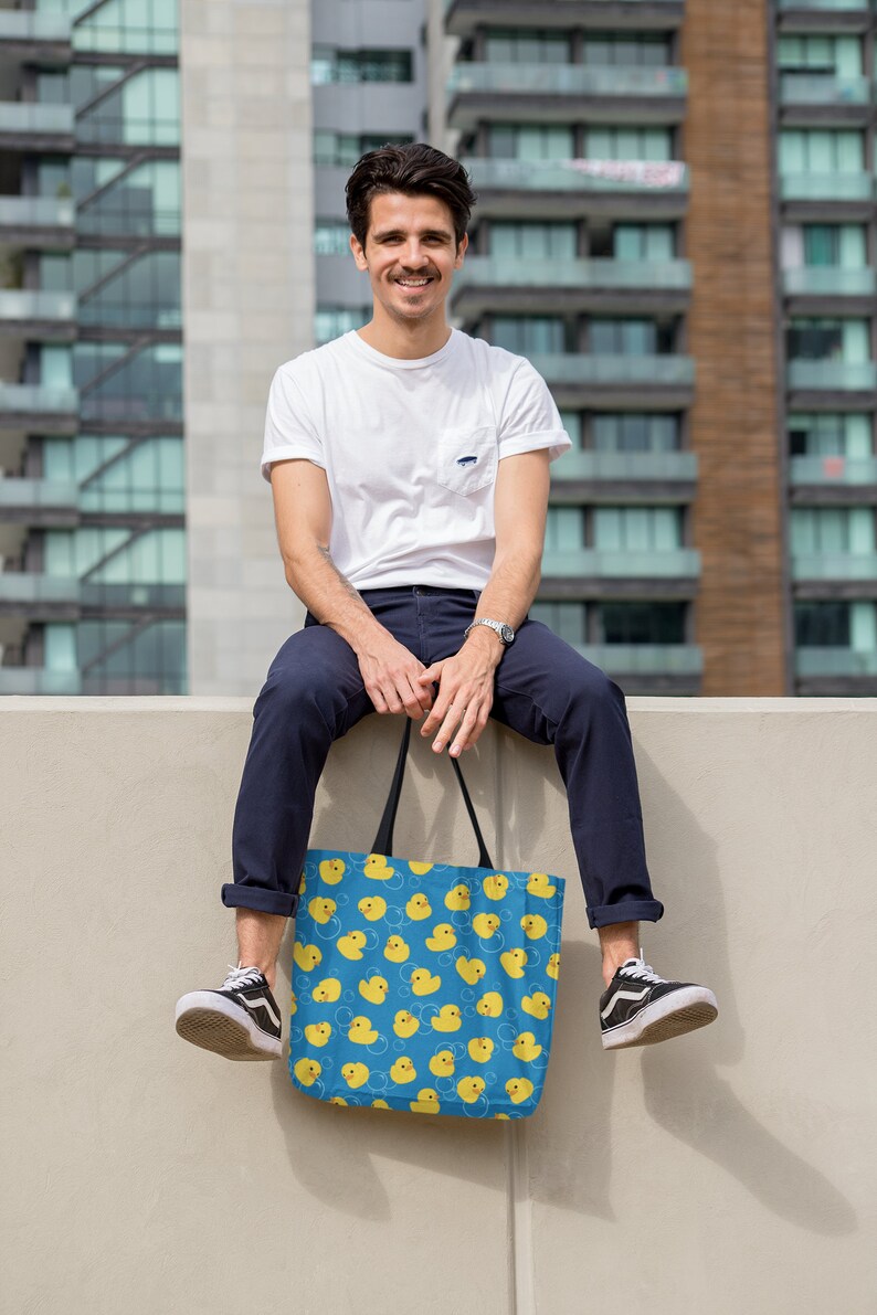 May include: A person sitting on a wall holding a blue tote bag with a yellow rubber ducky pattern.