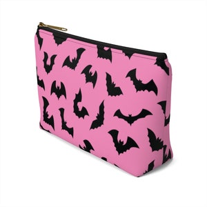 May include: Pink zippered makeup bag with a black bat pattern.