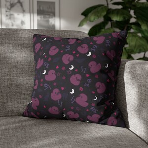 May include: A black throw pillow with a repeating pattern of purple rubber duckies, hearts, skulls, and crossbones. The background is black with white accents.