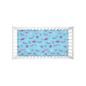 May include: A blue crib sheet with a pattern of pink and purple spaceships, green aliens, and white stars.
