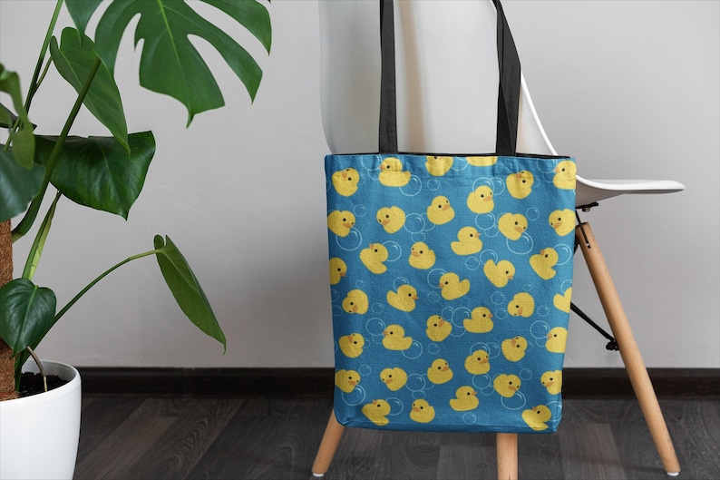 May include: A blue tote bag with a pattern of yellow rubber duckies and white bubbles. The bag has black handles.
