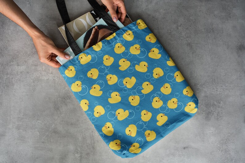 May include: A blue tote bag with a pattern of yellow rubber duckies and white bubbles. The bag has black handles and is filled with magazines.