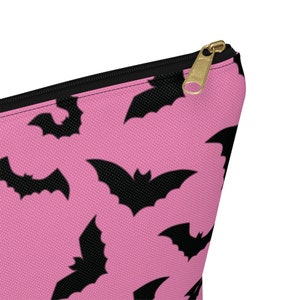May include: Pink zippered pouch with a black bat pattern. The pouch has a gold zipper pull.