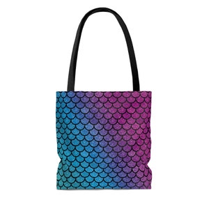 May include: A tote bag with a mermaid scale pattern. The scales are a gradient of pink, purple, blue, and teal. The bag has black straps.
