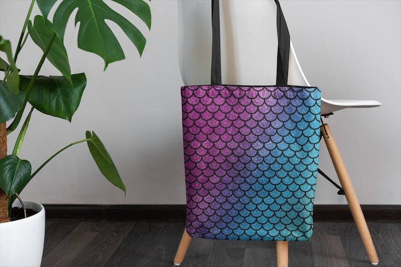 May include: A tote bag with a mermaid scale pattern in shades of pink, blue, and purple. The scales have a glittery finish.