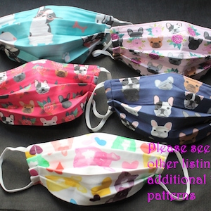 May include: Five face masks with white elastic ear loops. The masks feature various patterns of French Bulldogs on a teal, pink, red, navy blue, and white background. The text on the image says "Please see my other listing for additional Frenchie patterns."