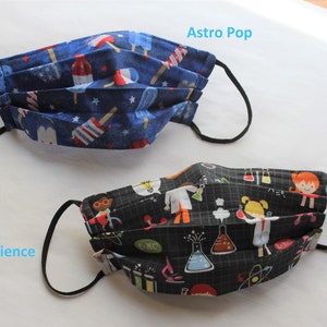 May include: Two fabric face masks with black elastic ear loops. The first mask has a blue background with red, white, and blue popsicle designs and the text "Astro Pop". The second mask has a black background with a science theme and the text "Weird Science".