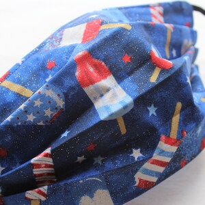 May include: Blue fabric face mask with a red, white, and blue popsicle print. The fabric has a glittery texture.