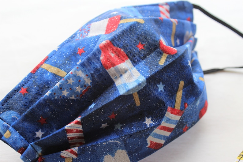 May include: Blue fabric face mask with a red, white, and blue popsicle print. The fabric has a glittery texture.