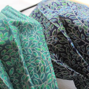 May include: Two face masks with a leafy pattern. One mask is teal with green leaves and the other is navy blue with green leaves.