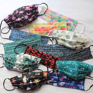 May include: A collection of 12 colorful fabric face masks with various patterns, including flamingos, pineapples, peacocks, and stars. The masks are pleated and have black elastic ear loops.