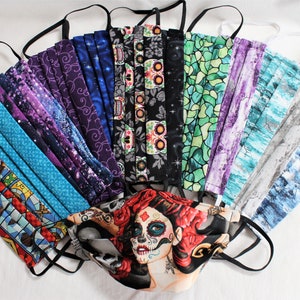 May include: A collection of 14 colorful fabric face masks with various patterns, including a Harry Potter themed mask, a skull and floral mask, and a stained glass pattern mask. The masks are arranged in a fan shape with the straps facing outwards.