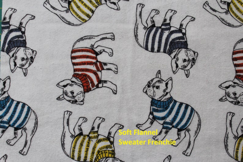 May include: White flannel fabric featuring a repeating pattern of French Bulldogs wearing striped sweaters in various colors. The text "Soft Flannel Sweater Frenchie" is visible in yellow.