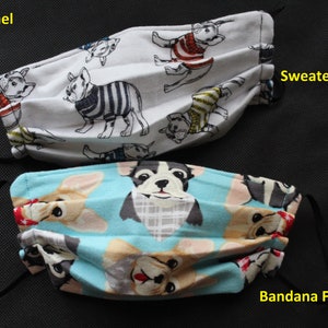 May include: Two face masks with black elastic ear loops. One mask is white with French bulldog illustrations wearing sweaters. The other is light blue with French bulldog illustrations wearing bandanas. Text on the masks reads "Soft Flannel", "Sweater Frenchie", and "Bandana Frenchie".