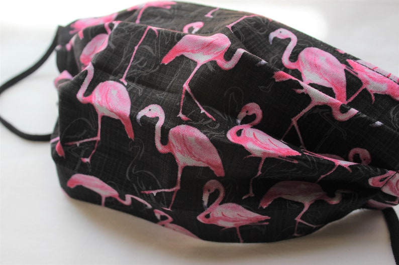 May include: Black face mask with a pink flamingo print. The mask has elastic ear loops.