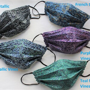 May include: Five different fabric face masks with a leaf pattern. The masks are pleated and have black elastic ear loops. The masks are labeled with the following names: Black Metallic Vines, Navy Metallic Vines, Purple Metallic Vines, Teal Metallic Vines, and French Quarter.