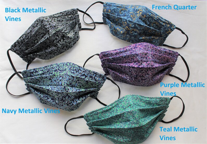 May include: Five different fabric face masks with a leaf pattern. The masks are pleated and have black elastic ear loops. The masks are labeled with the following names: Black Metallic Vines, Navy Metallic Vines, Purple Metallic Vines, Teal Metallic Vines, and French Quarter.