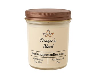 Può includere: Una candela in barattolo di vetro con coperchio in bronzo. L'etichetta recita "Dragon's Blood" con un motivo floreale e "Rockridgecandles.com". La parte inferiore dell'etichetta indica "All Natural Soy Wax" e "Handmade with Love".
