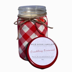 May include: A red and white checkered mason jar candle with a brown twine bow. The lid is red with a white label that reads "Rock Ridge Candles 100% hand poured soy candles Crackling Firewood Made with Fragrance Oils 16oz".