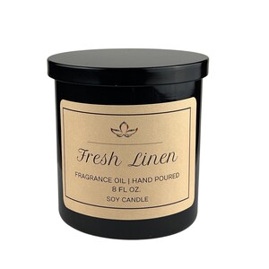 以下が含まれることがあります： 黒いガラス製のキャンドルジャー。ブラウンのラベルには「Fresh Linen」と「Fragrance Oil | Hand Poured 8 fl. oz. Soy Candle」と書かれています。
