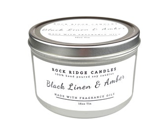 Puede incluir: Una vela en una lata de plata con una etiqueta blanca que dice "Rock Ridge Candles 100% hand poured soy candles Black Linen & Amber Made with Fragrance Oils 16oz Tin"