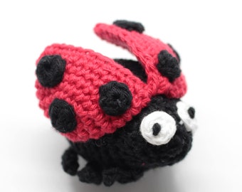 Puede incluir: Un juguete de crochet de mariquita rojo y negro con ojos blancos. La mariquita tiene manchas negras en su caparazón rojo.