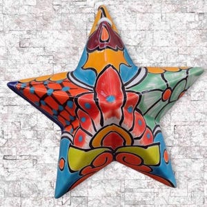 May include: A vibrant, hand-painted ceramic star with a glossy finish. The star features a colorful floral design in shades of red, orange, yellow, blue, and green, outlined in black. The star is a decorative item.