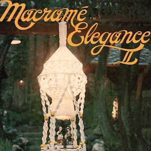 May include: A white macrame hanging plant holder with multiple tiers, featuring knotted cord patterns, yellow beads, and tassels. The text Macrame Elegance II, De Lune, and Basic to Advanced Designs Including Macrame Necklaces is printed on the cover.