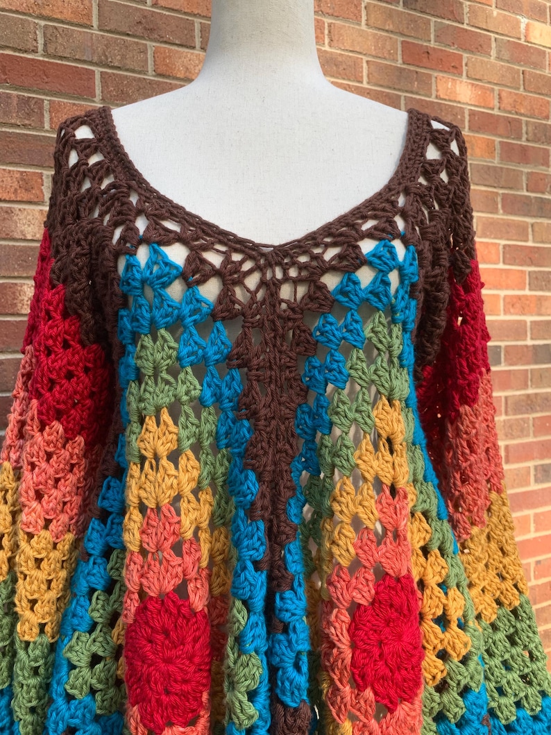 Op de afbeelding: Een kleurrijke gehaakte top met een diepe V-hals en lange mouwen. De top heeft een patchwork ontwerp in bruin, rood, oranje, geel, groen en blauw. De open weefselstructuur zorgt voor een licht en luchtig gevoel, perfect voor een bohemien stijl.
