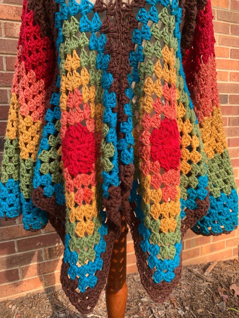 Op de afbeelding: Een handgemaakt gehaakt vest in een granny square patroon. Het open vest heeft een levendige mix van rode, oranje, gele, groene, blauwe en bruine tinten. De mouwen en het lichaam zijn versierd met een herhalend geometrisch ontwerp.