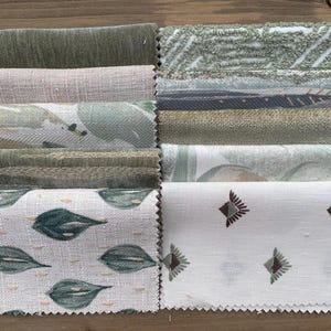 May include: A selection of fabric swatches in shades of green and neutral colours. The samples display diverse textures and patterns, including leaf and geometric designs. The fabrics are arranged on a wooden surface, providing a natural backdrop.