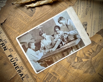 Puede incluir: Una fotografía antigua en blanco y negro de cuatro personas trabajando en una mesa. La imagen es de una postal con el texto "BLUFFTON, OHIO" y "PHOTOGRAPHY" impreso en ella.