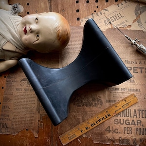 May include: A black, sculptural object with a flared base and a curved top, possibly a vintage display stand. The image includes a vintage doll, an antique syringe, and a wooden ruler.